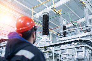 Electrical engineer worker inspects electrical substation with high voltage switches, wires, transformer and ceramic insulators.